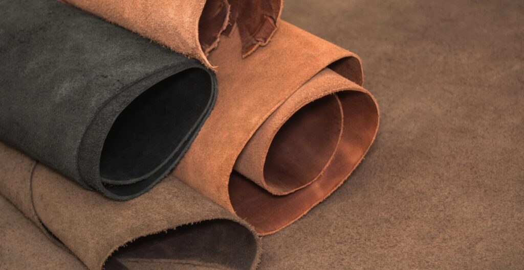 Rolls of various full grain leather in colors including brown, black, and tan, arranged on a flat surface