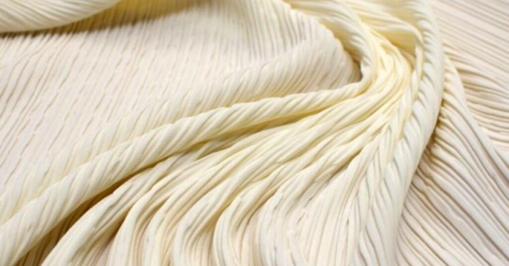 Close-up of cream-colored pleated polyamide fabric with a soft texture and elegant drape.