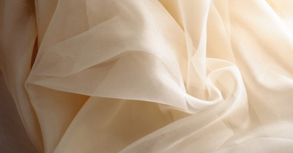 Sheer and lightweight beige organdy fabric with a crisp texture and elegant drape
