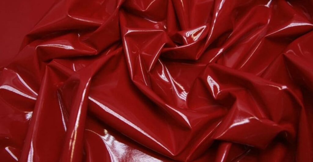 A close-up of crumpled, shiny red patent leather fabric, showing its glossy surface and distinctive folds.