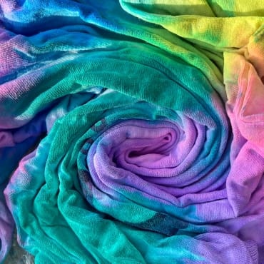 A vibrant, multicolored cotton fabric with a rainbow gradient, gently twisted into a spiral.