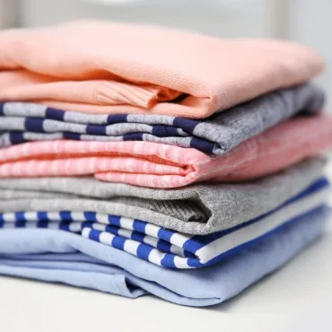 A neatly folded stack of cotton clothing in various colors, including pink, gray, and blue.