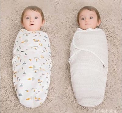 Two swaddled babies, one in a patterned blanket and the other in a plain white blanket, both looking surprised.
