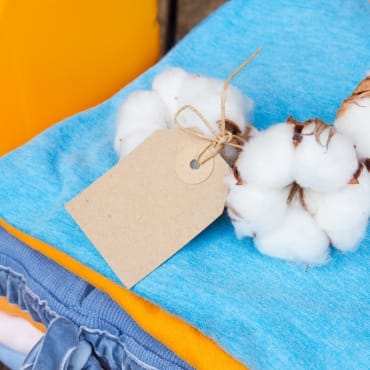 Cotton bolls and a blank tag resting on a stack of colorful cotton fabric.