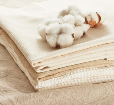 A neatly stacked display of various cotton fabrics in neutral tones, with a cluster of cotton bolls placed atop.