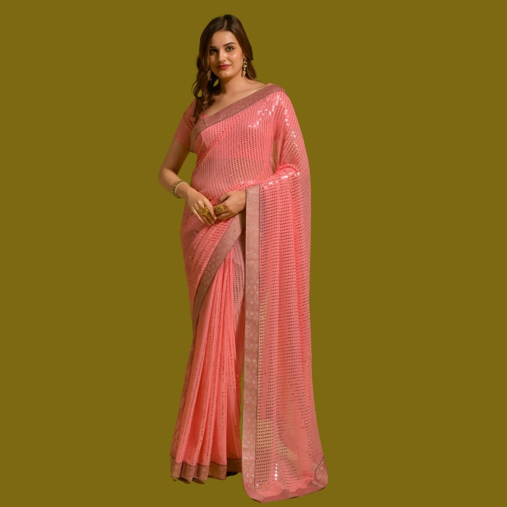 A woman wearing a stunning pink saree with shimmering embellishments, standing against a plain background, smiling softly at the camera.