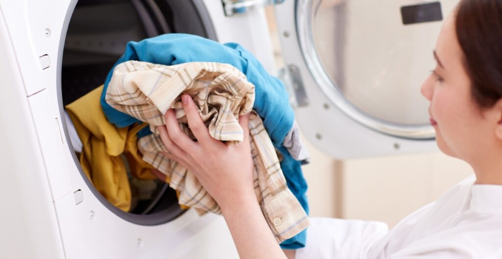 A person placing wrinkled clothes into a dryer.