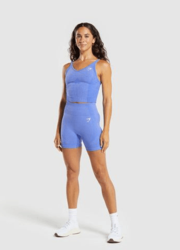 A young woman in a blue athletic outfit stands confidently, wearing a fitted sports bra and matching shorts.