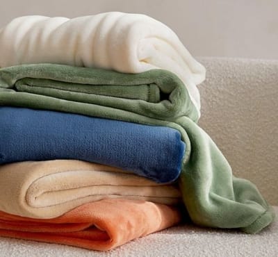 A neatly folded stack of colorful cotton fabric or clothing items, including white, green, blue, beige, and peach-colored pieces.