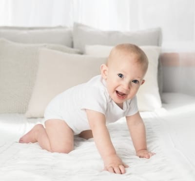 A baby crawling on a bed covered with soft pillows and blankets.