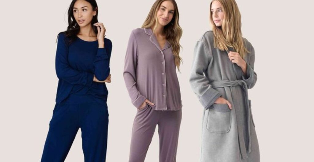 Three women wearing different styles of loungewear: a navy long-sleeve top with matching pants, a lilac pajama set with buttons, and a gray robe.