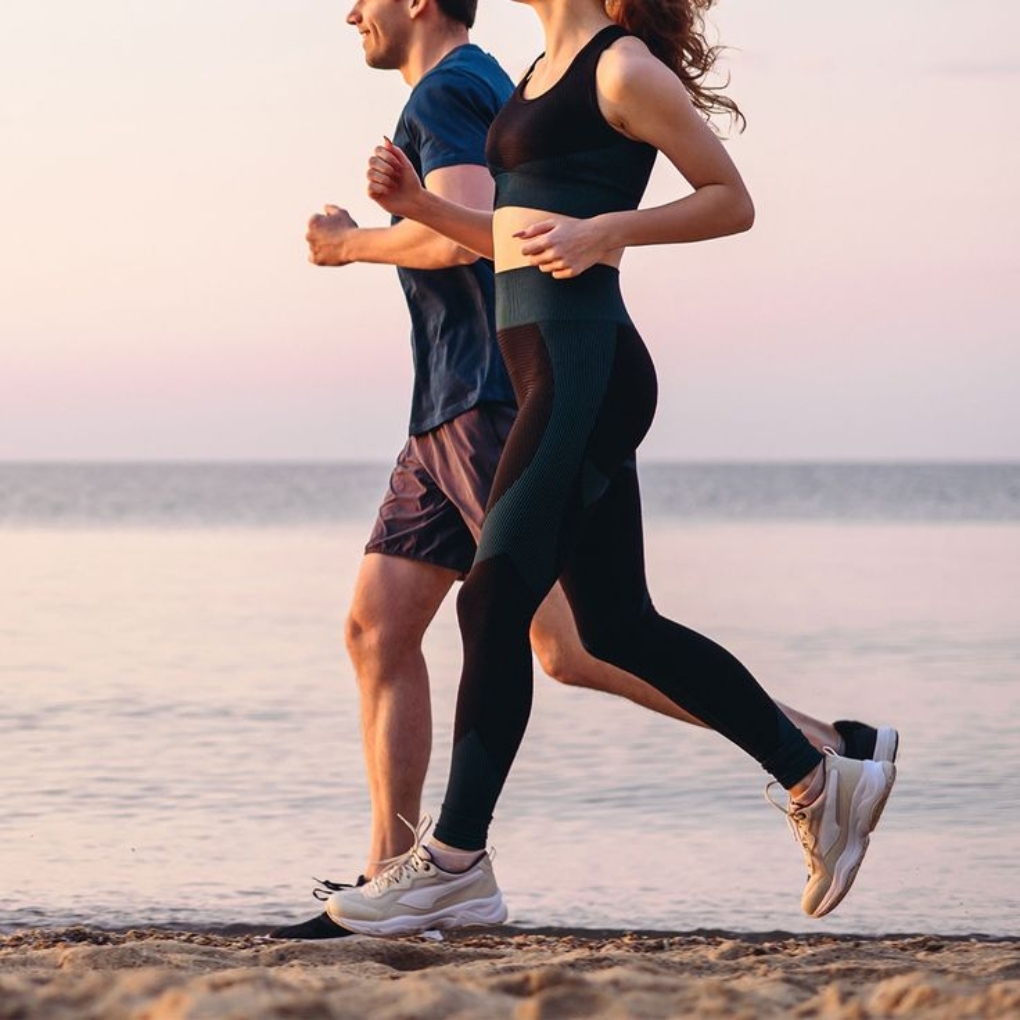 A man and woman jog together along a beach during sunset. The man wears a blue t-shirt and shorts, while the woman is dressed in a black sports bra and leggings.
Gymwear guid