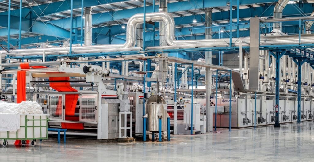 Modern textile manufacturing facility with automated machines processing red fabric and white textile rolls.