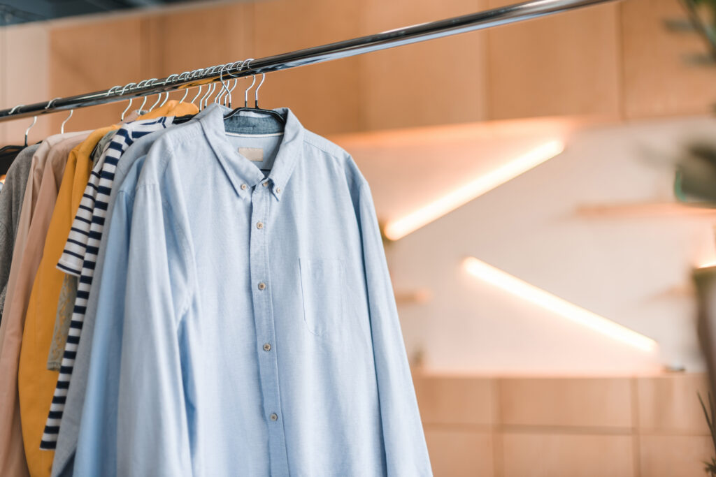 A close-up view of a selection of wrinkle-free shirts hanging on a rack, featuring various colors and patterns, with a blurred modern interior in the background. Wrinkle-Free Shirts