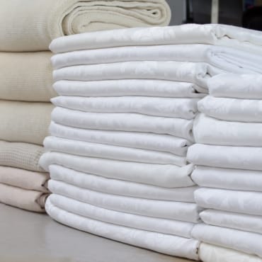 Neatly folded cotton sheets in various shades of white and cream.