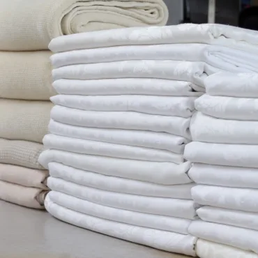 Neatly folded cotton sheets in various shades of white and cream.