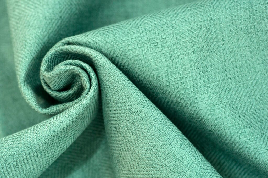 A textured, mint-green cotton fabric rolled into a spiral, highlighting its woven pattern.