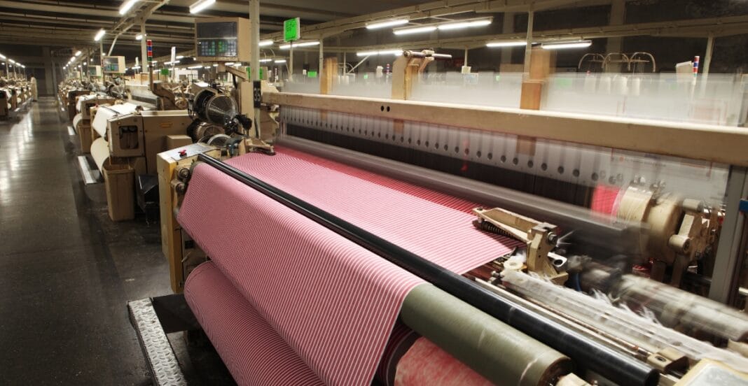 A textile mill with weaving machines producing striped fabric from cotton.
