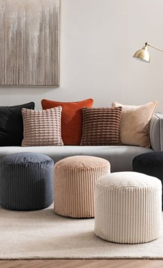 A cozy living room featuring a gray sofa with decorative pillows and several corduroy poufs in various colors on a light rug.