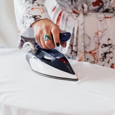 A close-up of a hand using a steam iron on a white fabric, showcasing the ironing process.