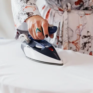 A close-up of a hand using a steam iron on a white fabric, showcasing the ironing process. 