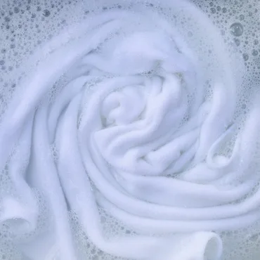 Close-up of white rayon fabric submerged in soapy water, displaying soft, swirling textures.