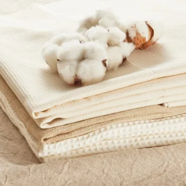 A stack of beige and cream-colored cotton fabrics with soft cotton bolls on top.