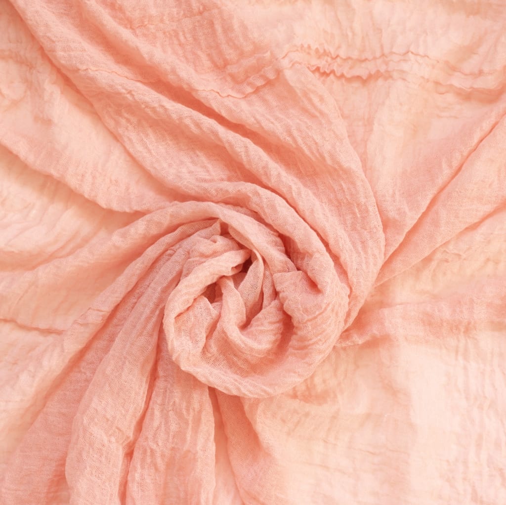 Close-up image of soft, peach-colored gauze cotton fabric, softly twisted in a swirl.