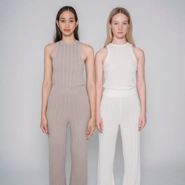 Two women standing side by side, wearing stylish, neutral-toned polyester outfits against a plain background.