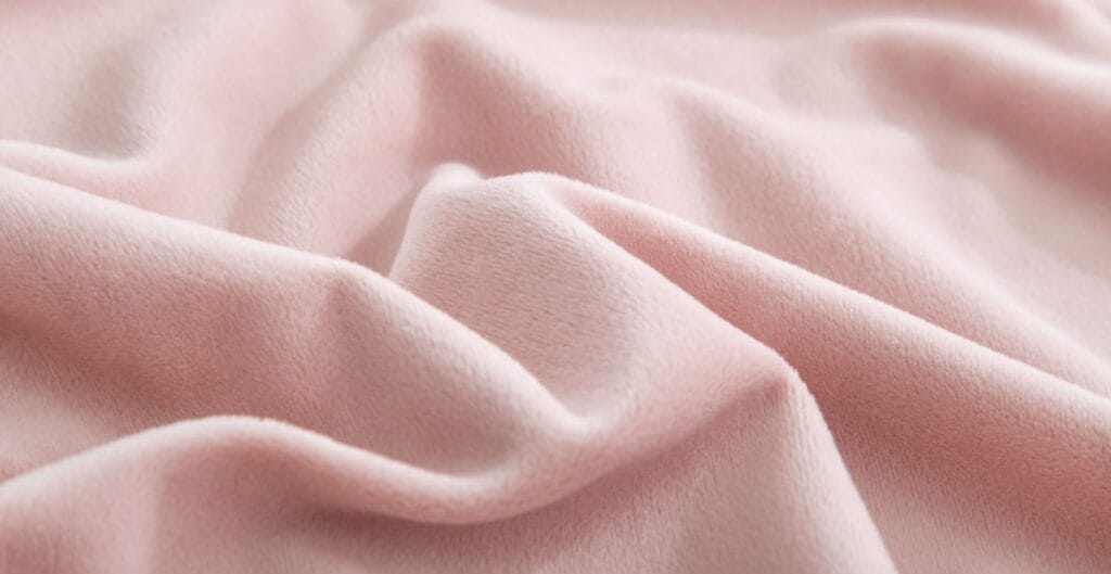 A close-up of soft, pastel pink fabric with gentle folds and a smooth, velvety texture.