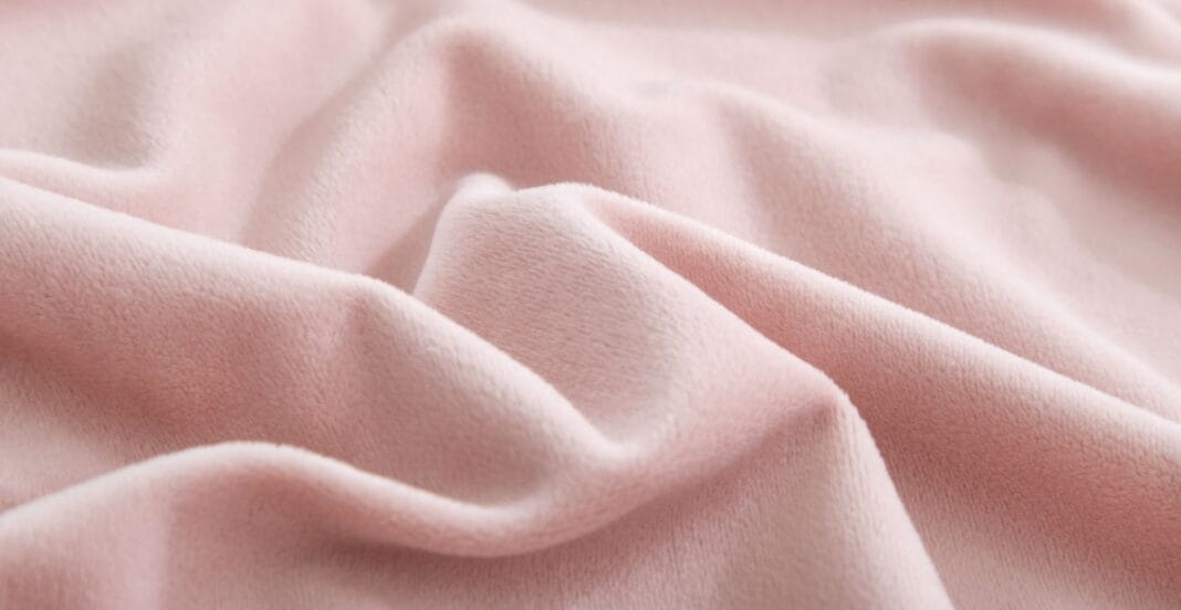 A close-up of soft, pastel pink fabric with gentle folds and a smooth, velvety texture.