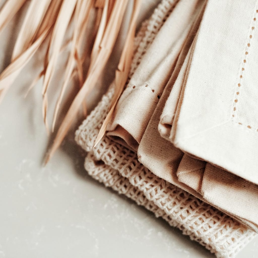 Close-up of folded beige and cream fabric textiles, showcasing different textures including woven and linen-like materials, arranged neatly on a light surface.