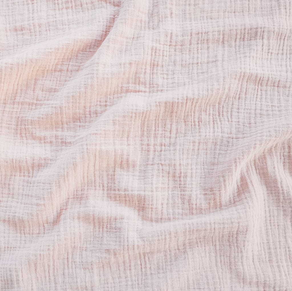 Close-up image of soft, lightweight cotton muslin fabric with gentle folds, showcasing its fine weave and delicate texture in light pink and white tones.