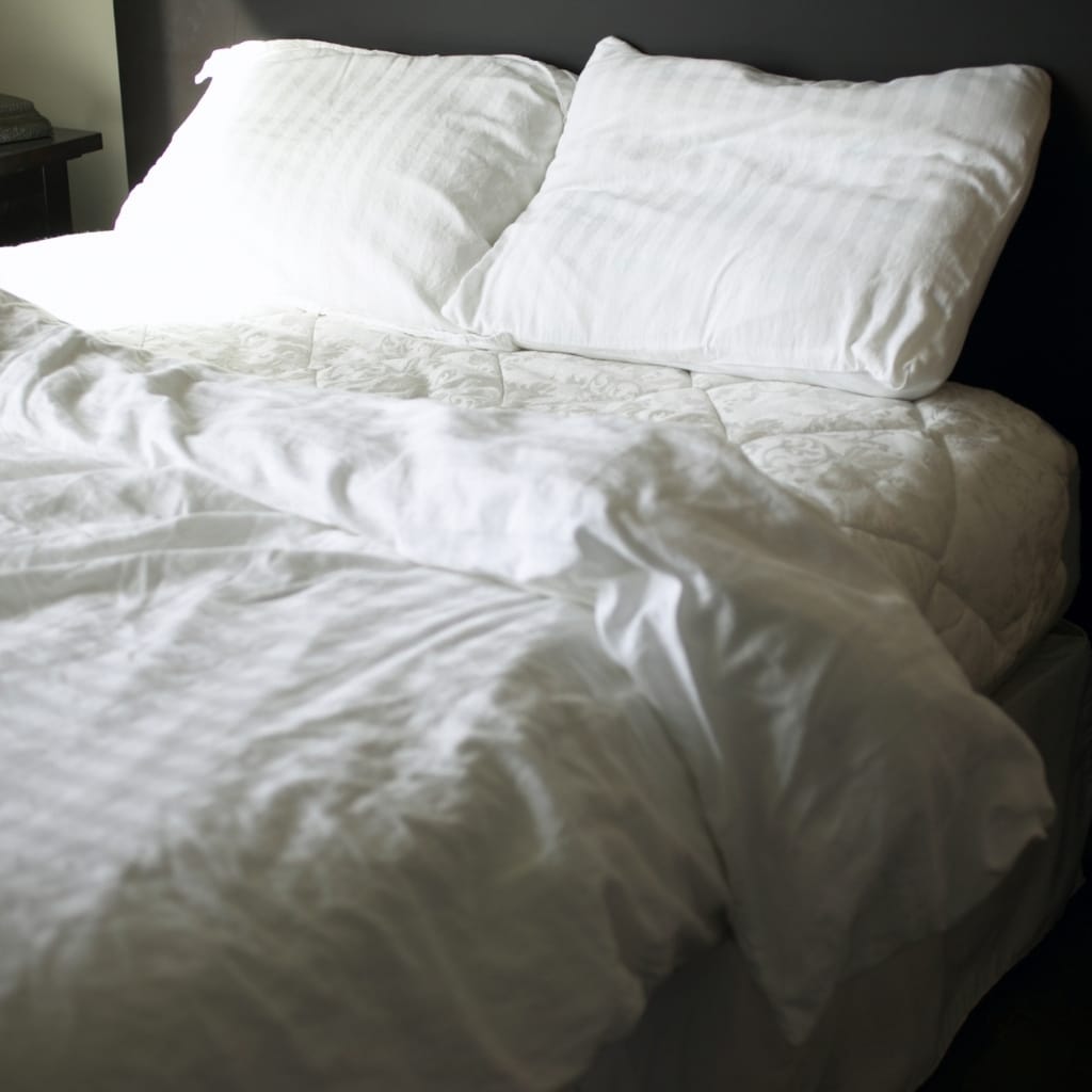 A neatly made bed with white bedding, including pillows and a comforter, in a bedroom with dark wall.