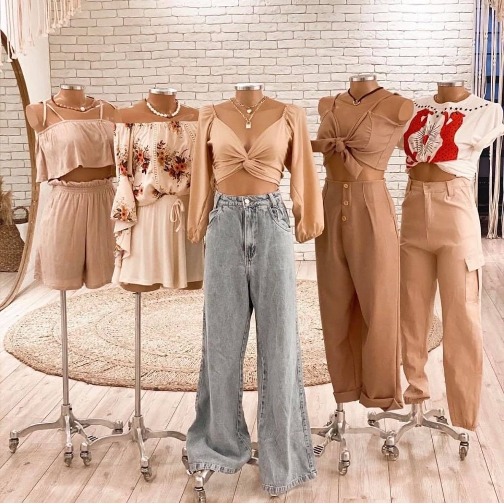 Group of six mannequin torsos dressed in various stylish, beige and neutral-toned women's outfits, displayed on rolling stands against a white brick wall. Cloth Made in USA