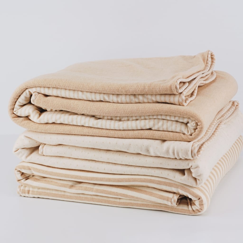 A neatly stacked pile of six beige and cream-colored cotton fabrics, folded uniformly.