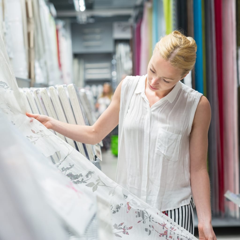 A woman shopping in a store, examining fabric or curtains on display.