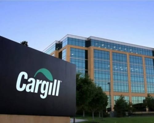 A modern office building with large glass windows and a prominent black sign in the foreground displaying the Cargill logo.