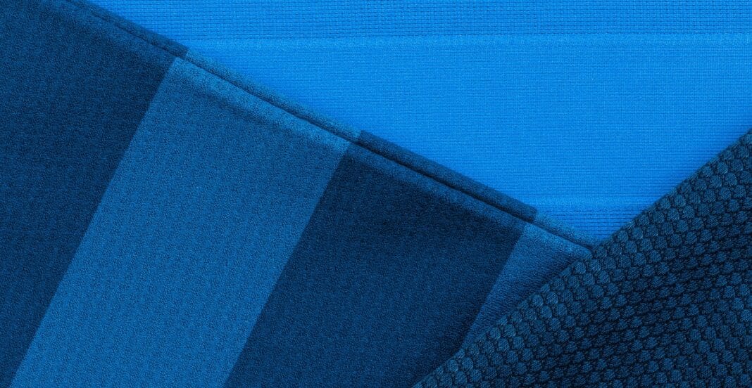 Close-up image of a textured, deep blue polyester knit fabric with a pattern of small, repeating hexagons and smooth sections.