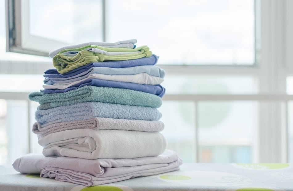 A neatly folded stack of clothes on a table near a window, with the background showcasing bright natural light.