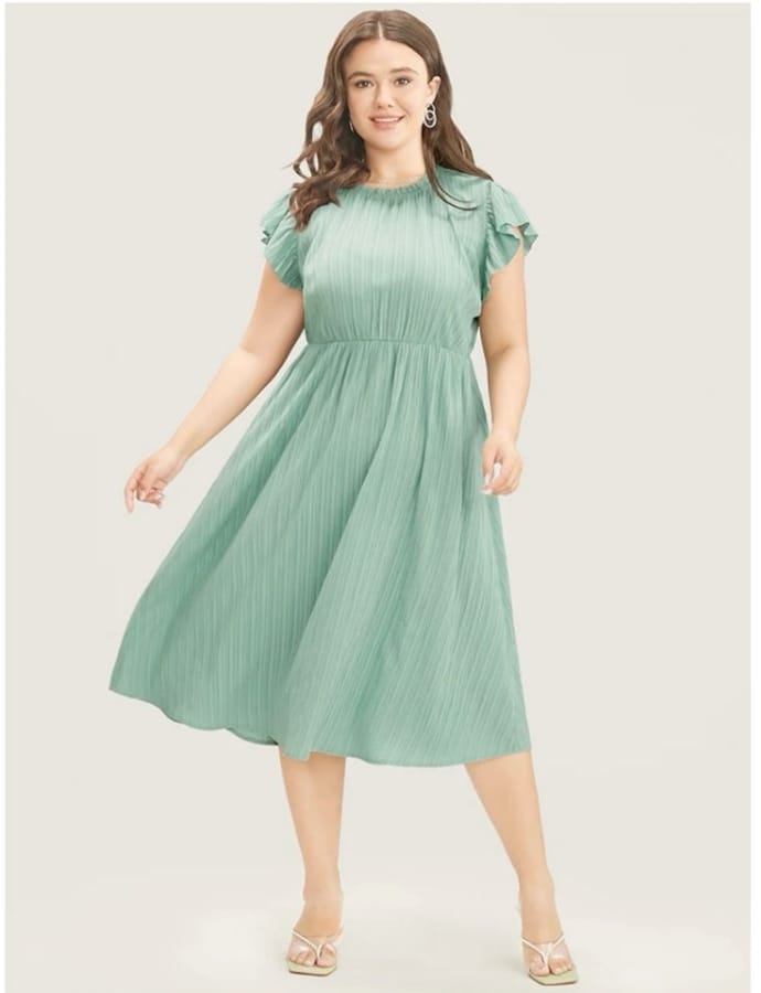 A woman wearing a mint green cotton babydoll dress with ruffled sleeves, standing against a plain background.