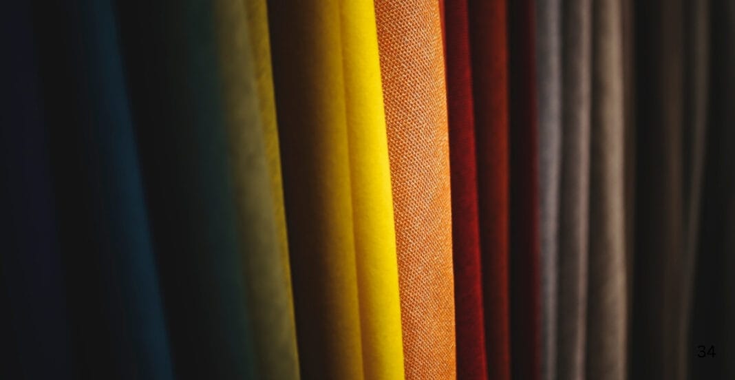 Close-up of vertically arranged colorful fabric swatches, primarily in shades of yellow, orange, red, and neutral tones.
