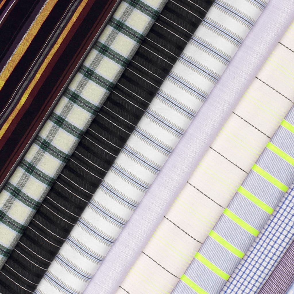 Assorted rolls of cotton fabric with various patterns and colors, including checkered, striped, and plain designs.