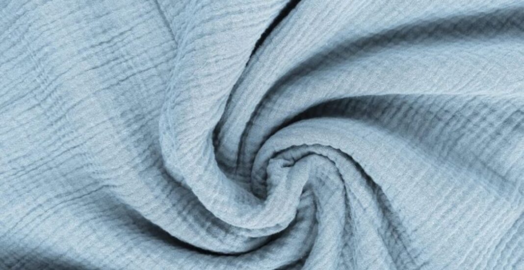 A close-up image of light blue cotton gauze fabric, twisted into a spiral. The fabric has a soft, airy, and textured appearance with a slightly wrinkled surface.