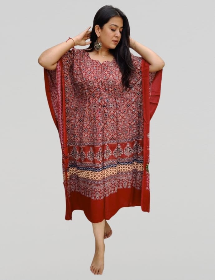 A woman wearing a red and patterned cotton kaftan dress, standing against a plain background with her hands near her head.