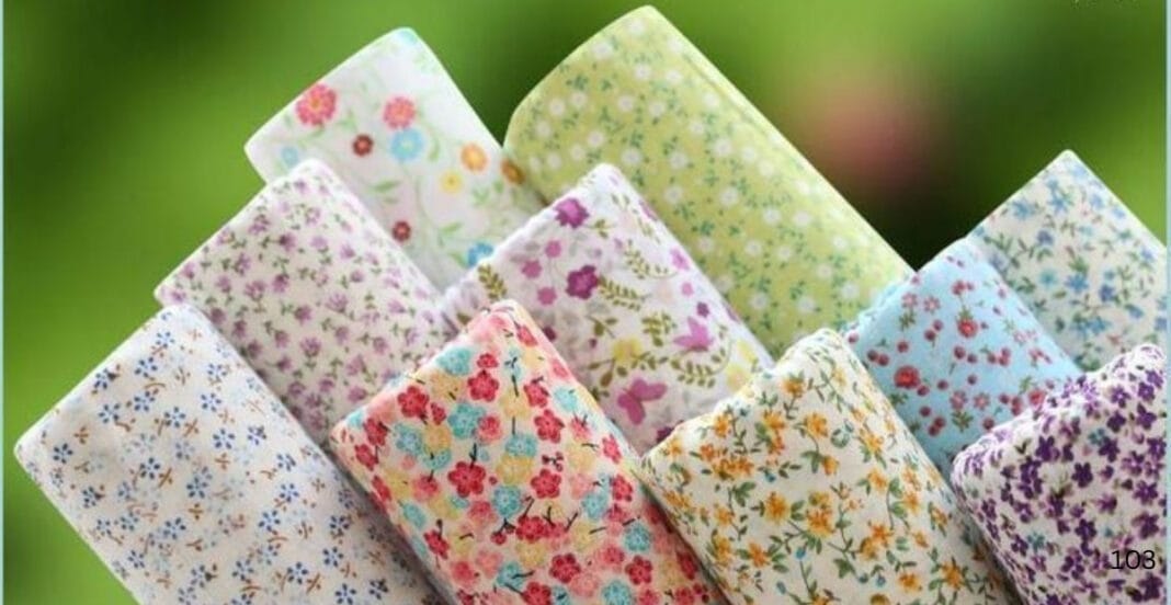 Close-up image of multiple folded pieces of colorful floral cotton lawn fabric with a blurred green background.