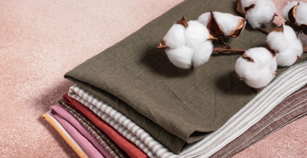 A stack of neatly folded fabrics in various patterns and colors, topped with cotton branches.