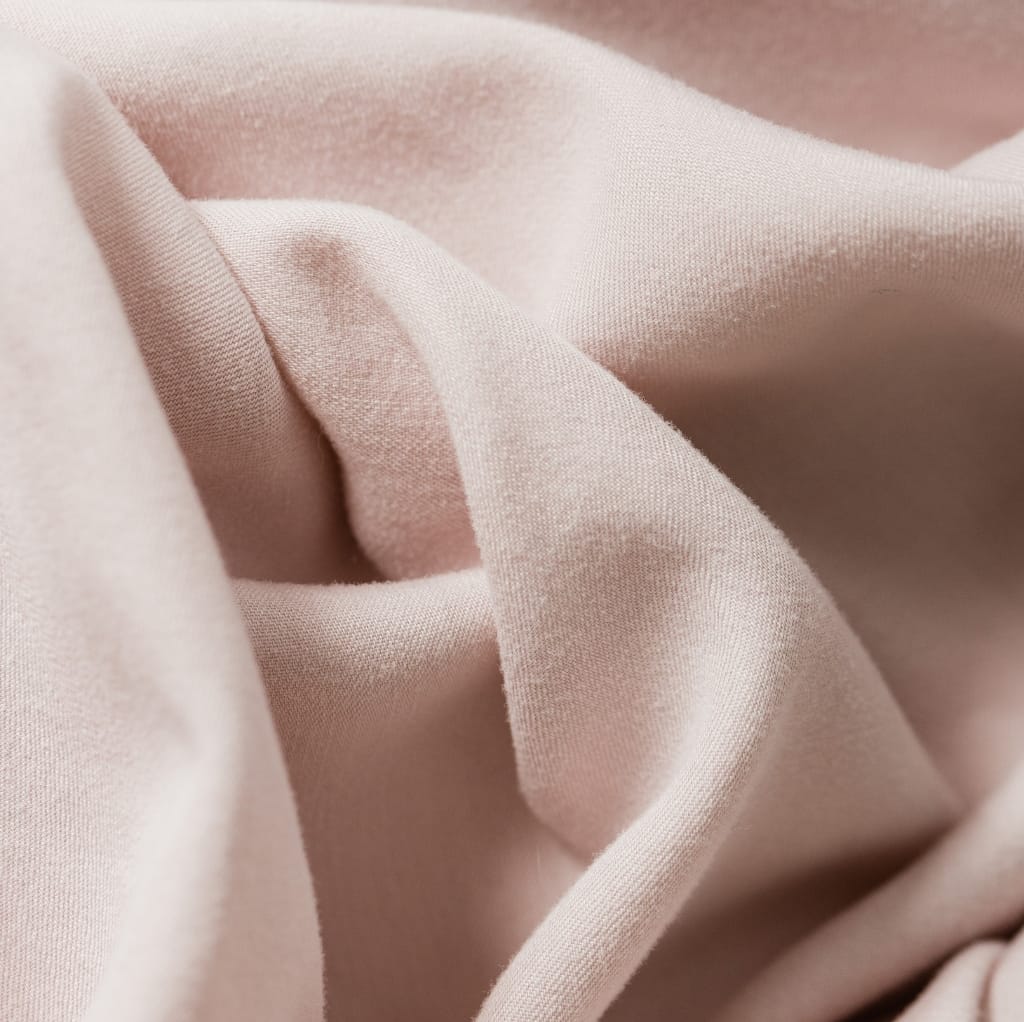 A close-up image of soft, pale pink cotton fabric with gentle folds and smooth texture.