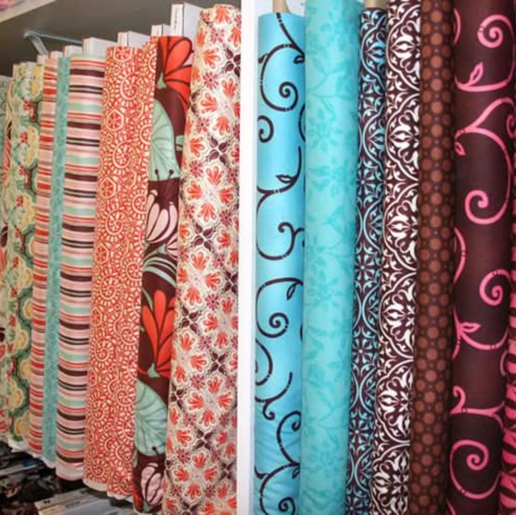 A display of colorful fabric rolls with various intricate patterns and designs, showcasing custom printed cotton fabric rolls in a fabric store.