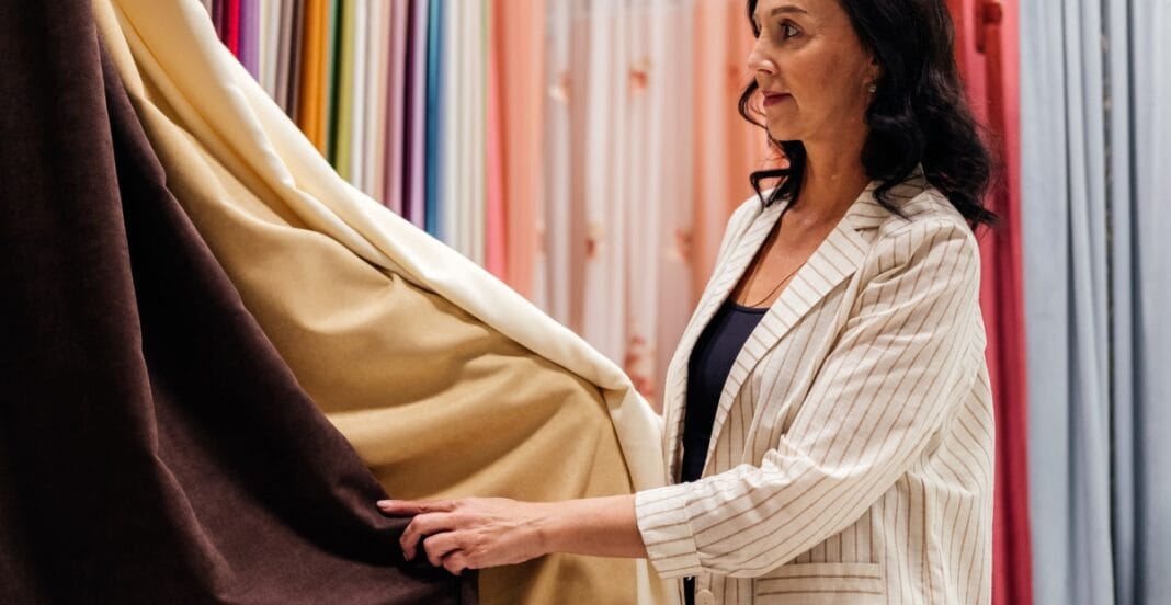 Woman examining different drapery fabric types in a curtain showroom.